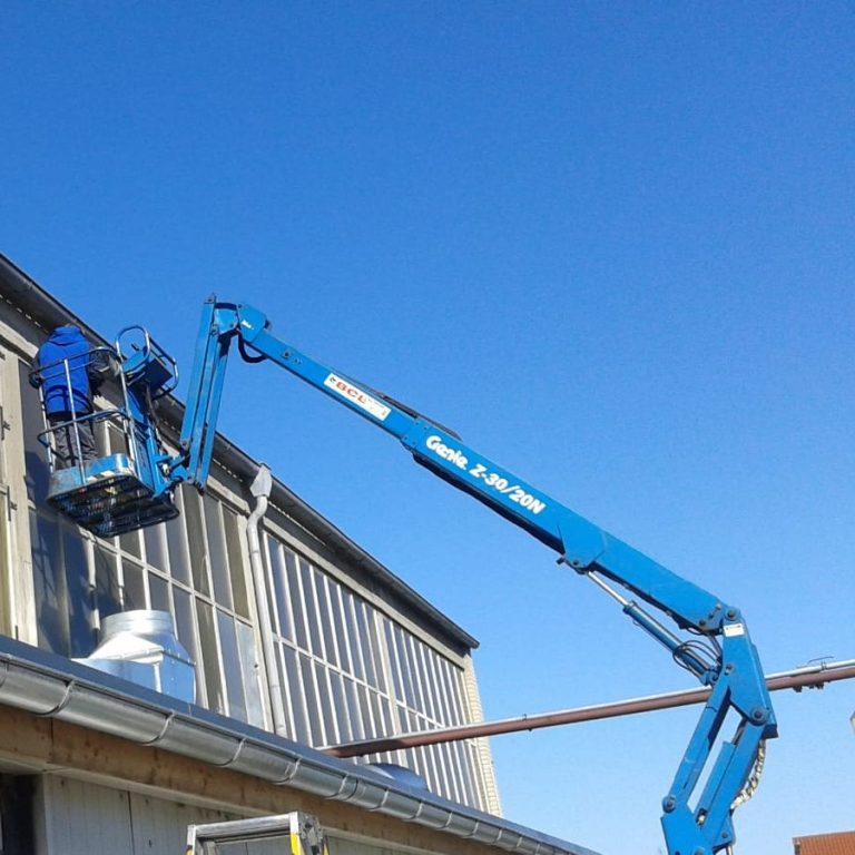 Zwei Arbeiter auf einer Hebebühne bei der Montage unter klarem Himmel.